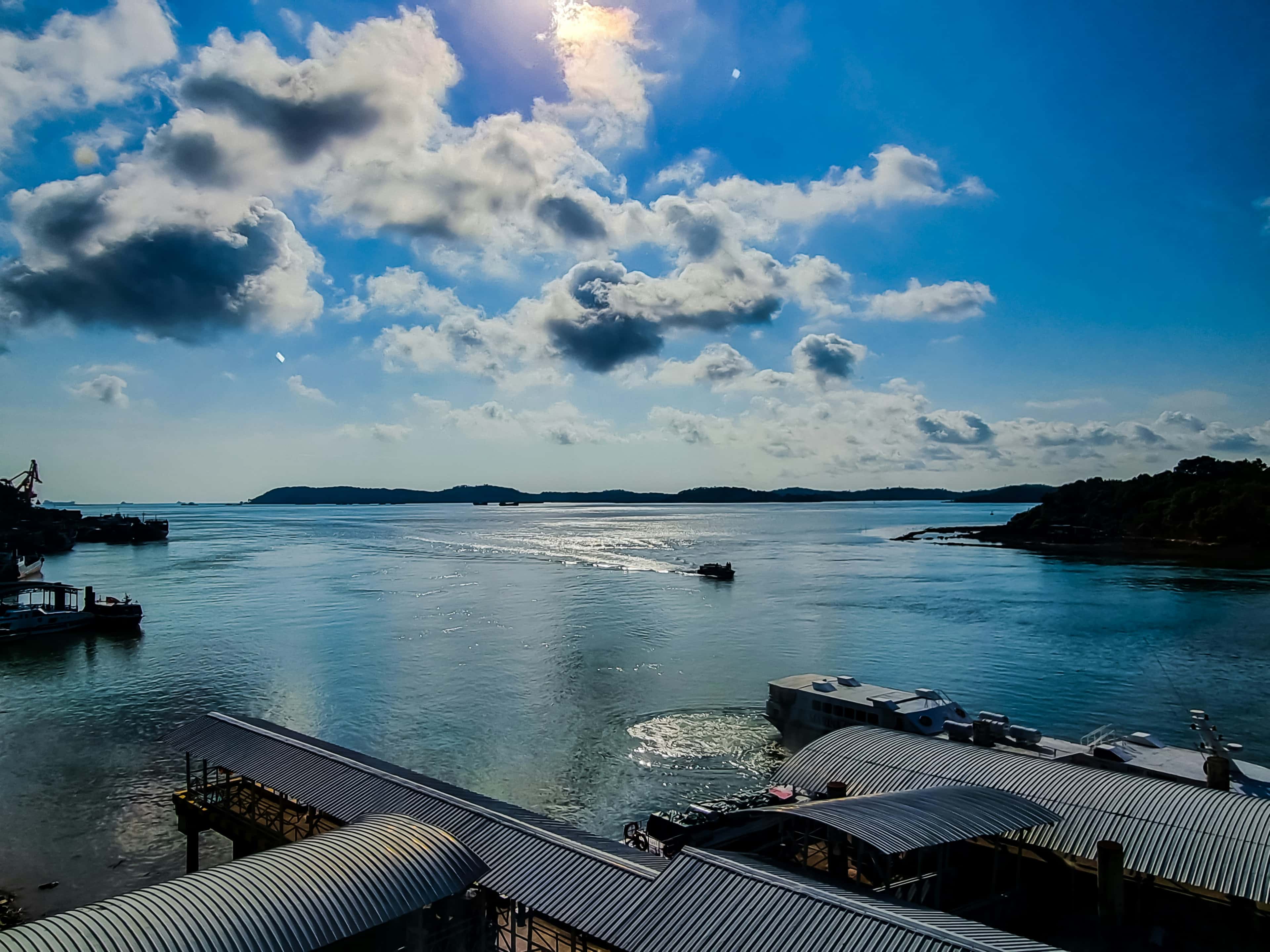 Sunlit Batam waterfront with traditional fishing kelongs and distant islands across a calm sea.