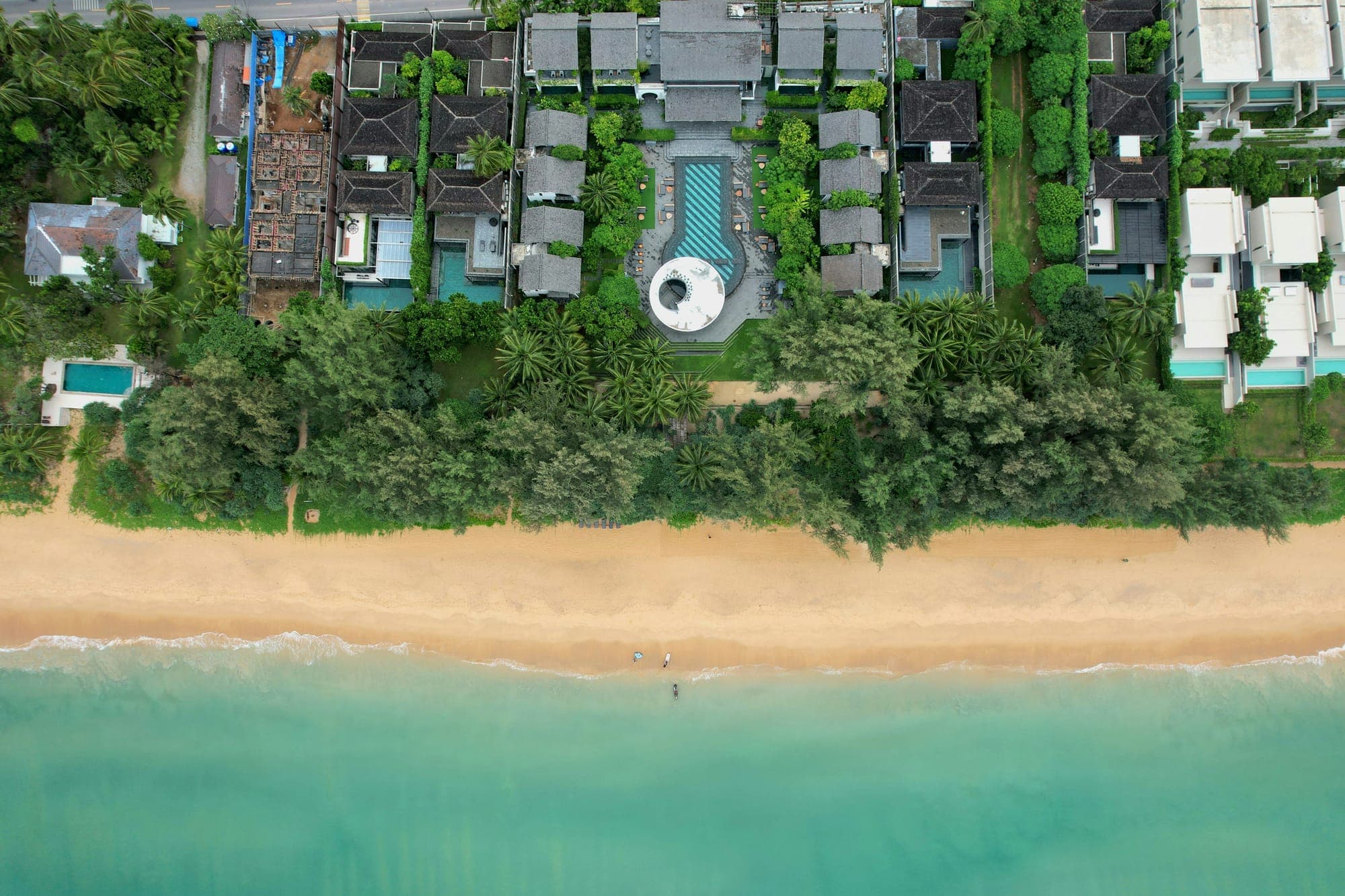 Aerial view of luxury beachfront villas with private pools along a tropical coastline